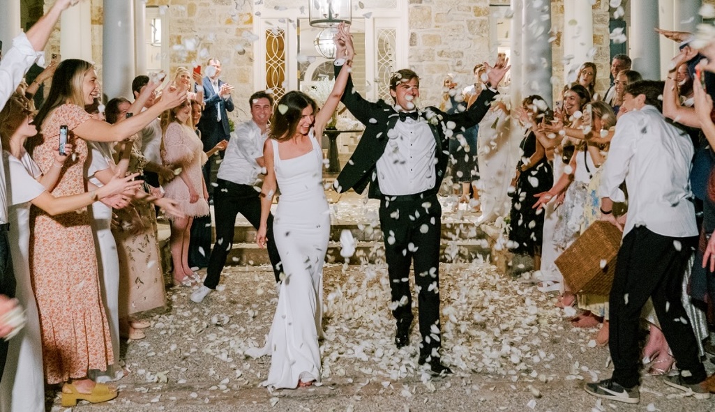 Newlywed couple being showered with flower petals by wedding guests.
