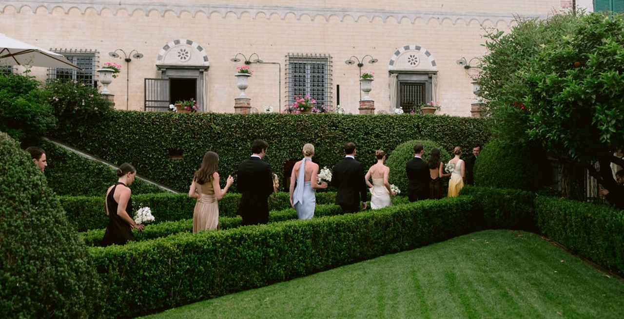 Wedding party walking through a garden with hedges.