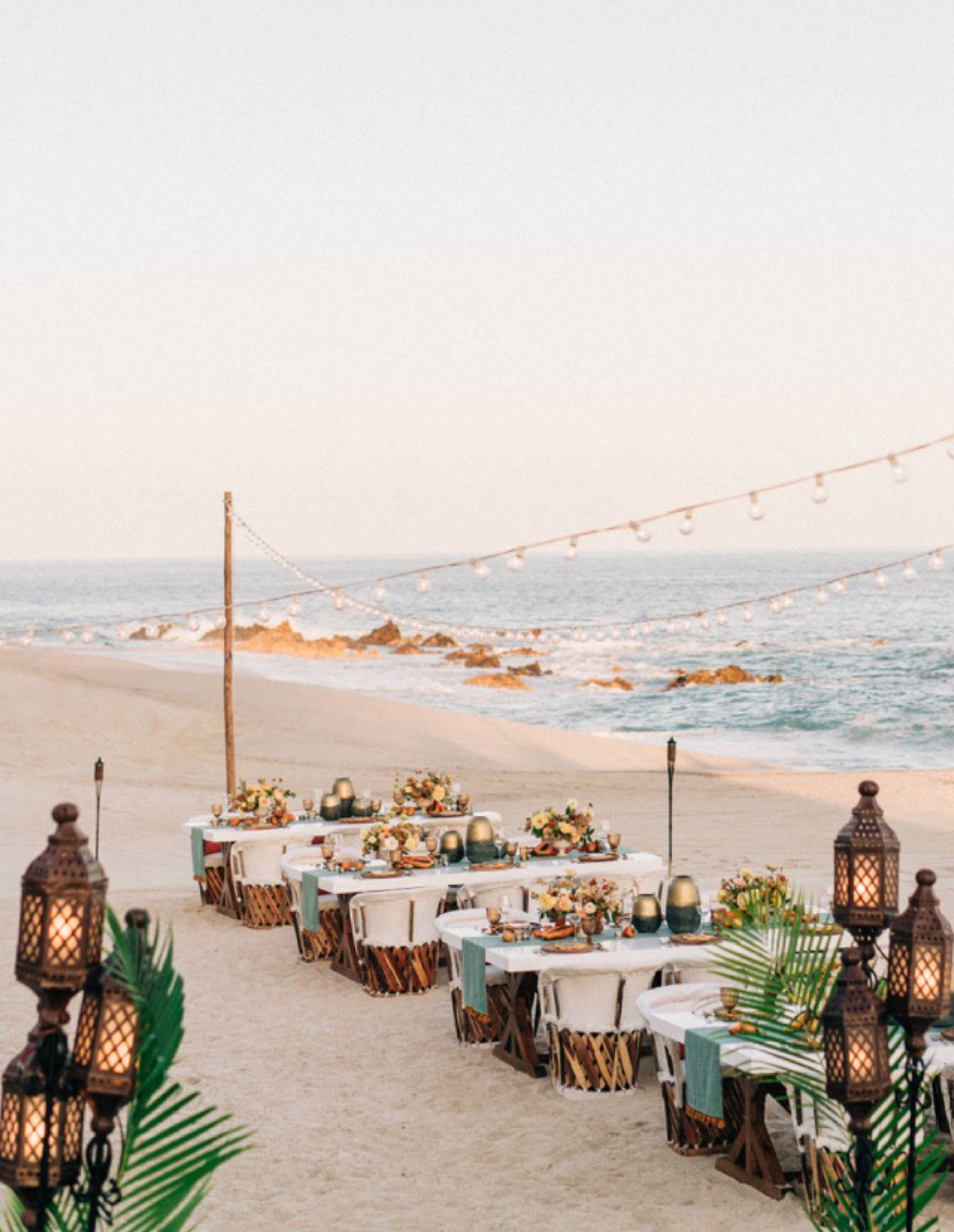 Reception tables on the beach with string lights above.